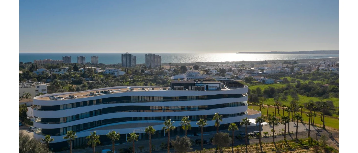 Striking white, curved tiered building reminiscent of a wave, surrounded by gardens with the ocean in the background 