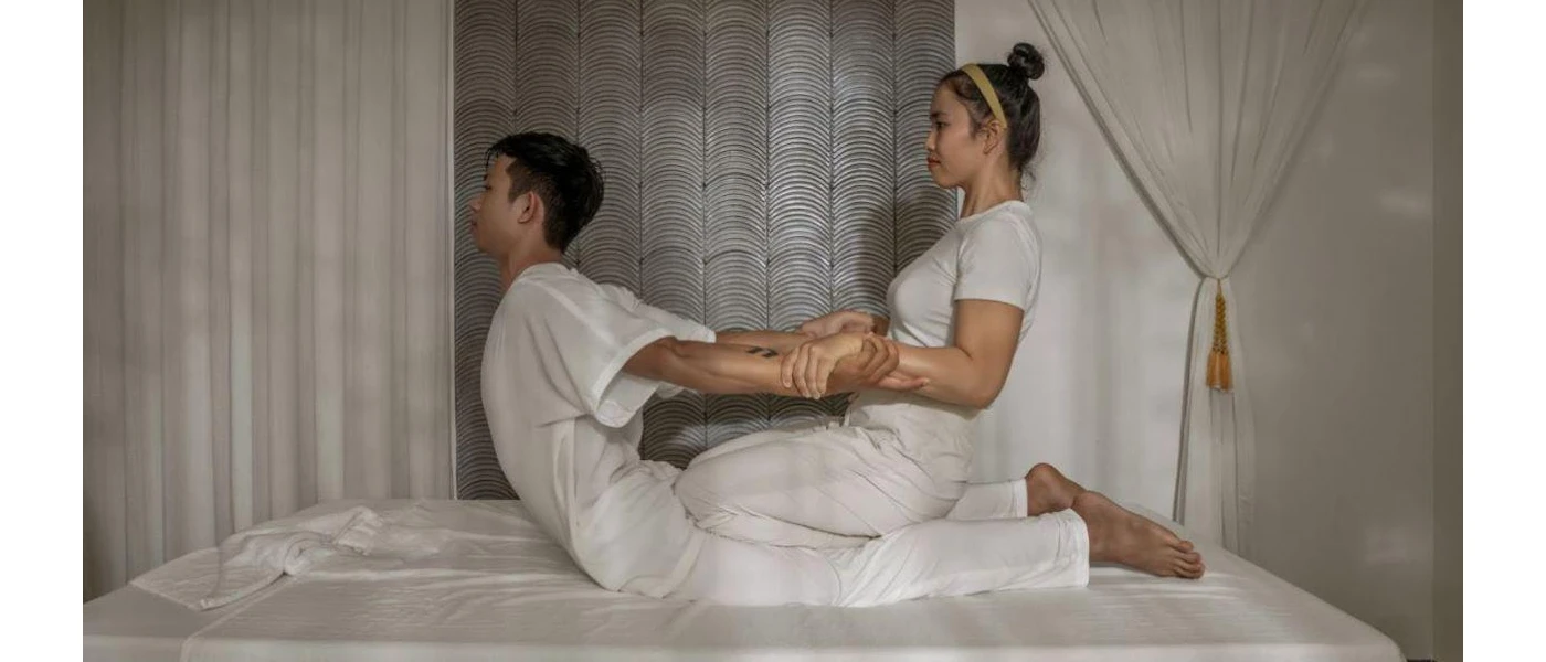Woman lies on her front as a therapist pulls her backwards by her arms, aiding a stretch