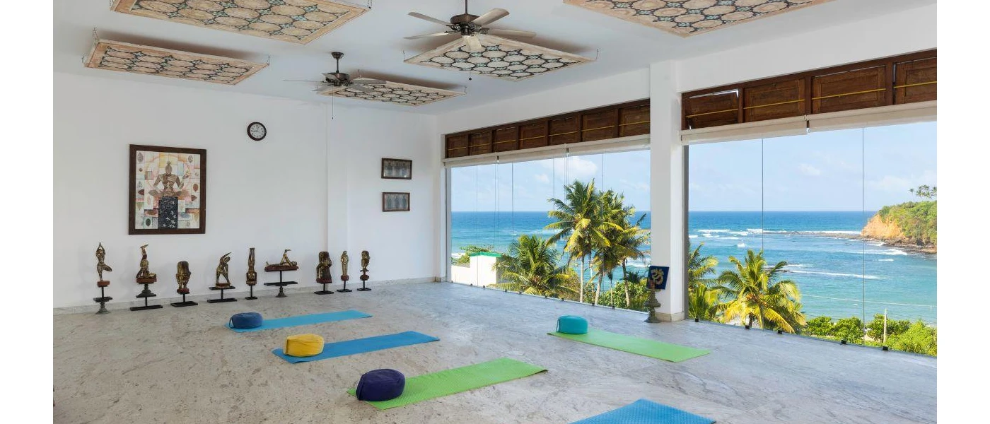 Beachfront yoga shala with floor-to-ceiling windows, bronze statues, dark-wood shutters and ceiling fans