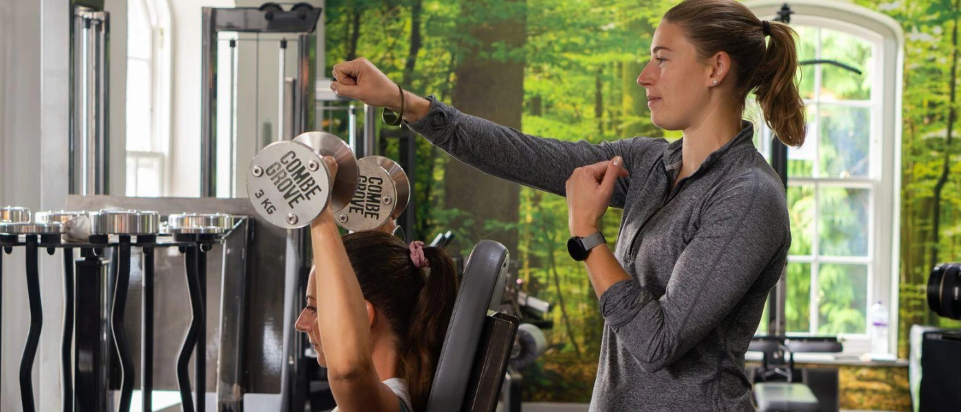 Woman working out in a gym with a personal trainer in attendance