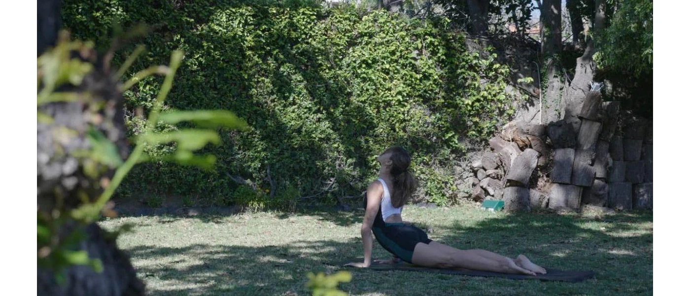 Woman in active wear in a yoga pose in a leafy garden with the sun rays peeking through