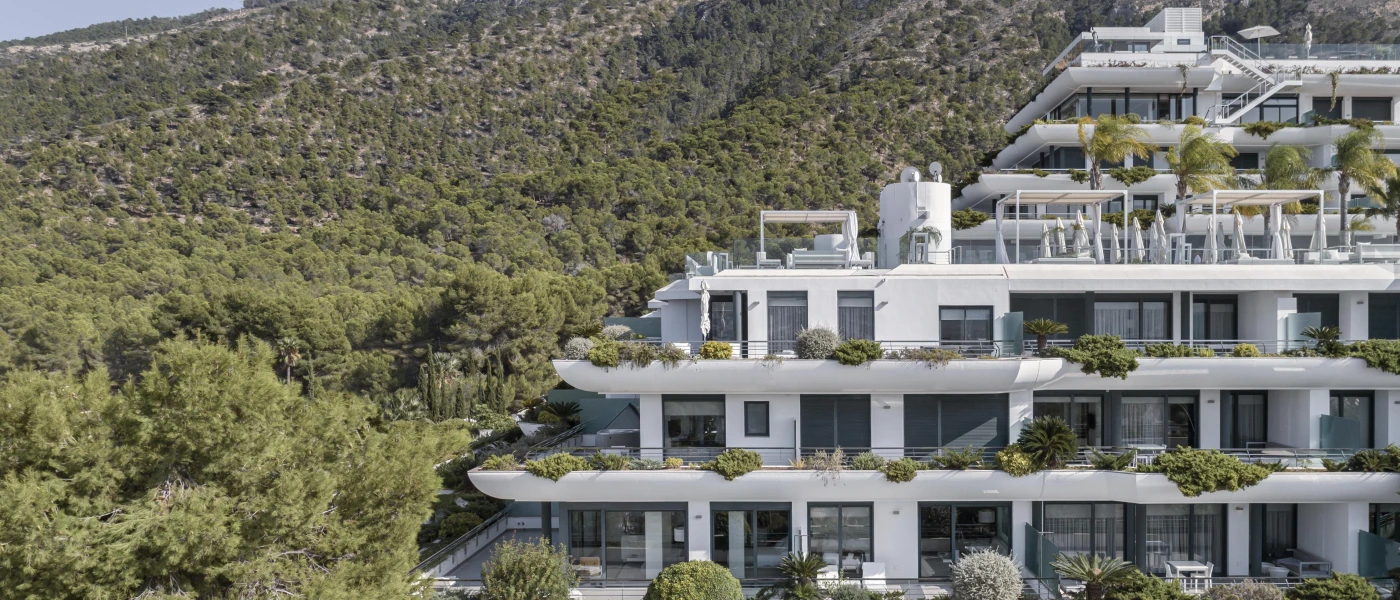 Tiered white building adorned with shrubs on a leafy hillside