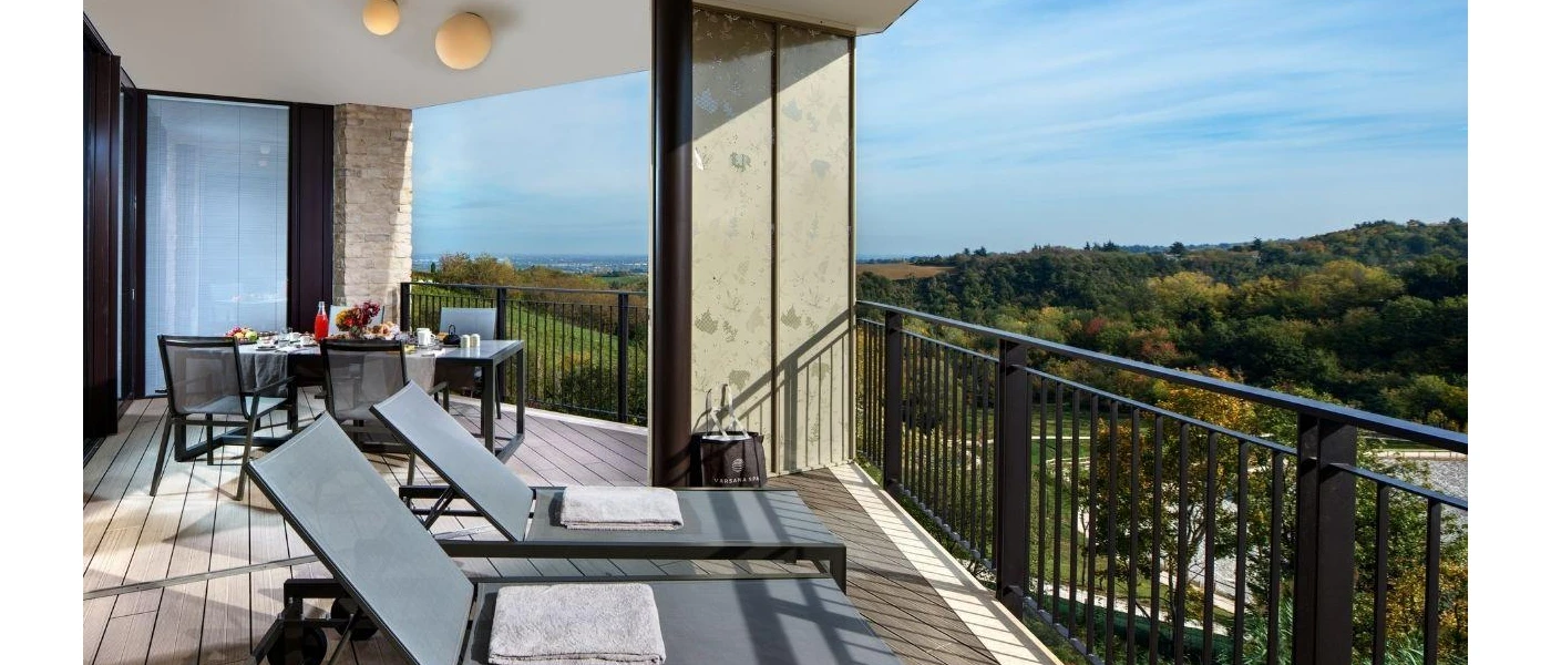 Balcony with black railings, wooden decking, two black loungers and a table and chairs made up with food and drink