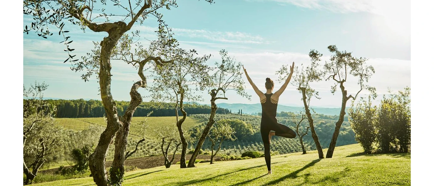 Woman in black active wear in a yoga pose outdoors overlooking vineyards and olive groves