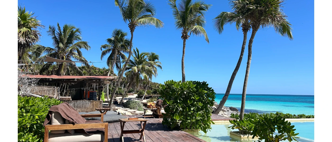 Wooden sea-facing terrace with wooden furniture, palm trees and a swimming pool overlooking the sea