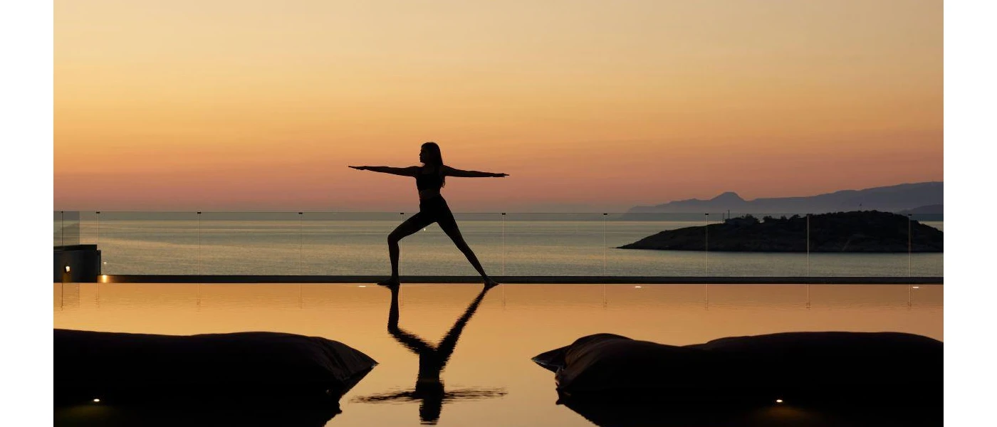 Silhouette of a woman in a yoga pose at sunrise or sunset next to an ocean-facing pool