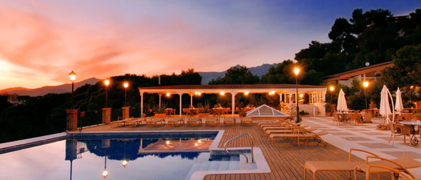 Sunset over a wooden terrace with a rectangular swimming pool and surrounding greenery