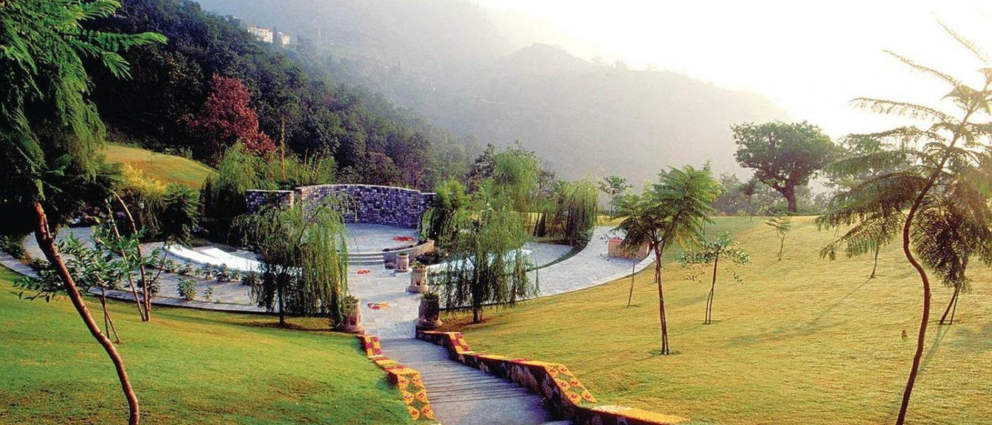 Stone steps leading through manicured lawns to a stone-walled patio, with views of the misty Himalayas
