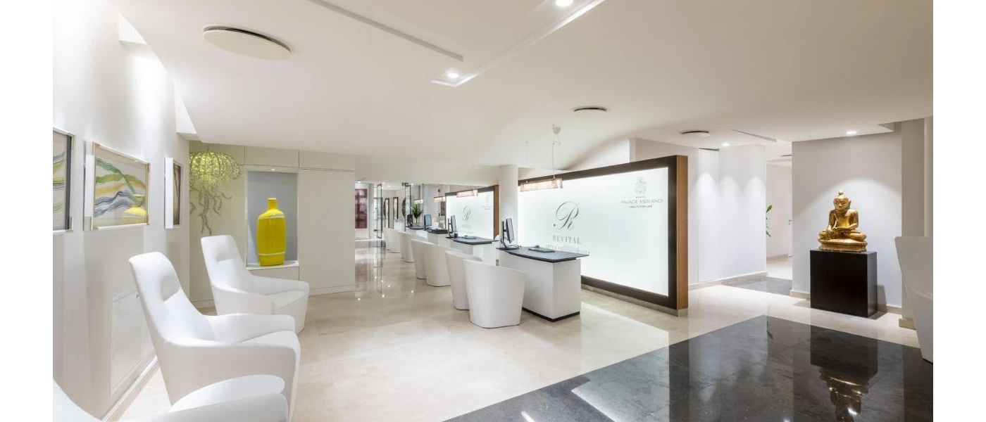 Elegant white spa area with glossy tiled floor, a gold Buddha statue and a white reception desk