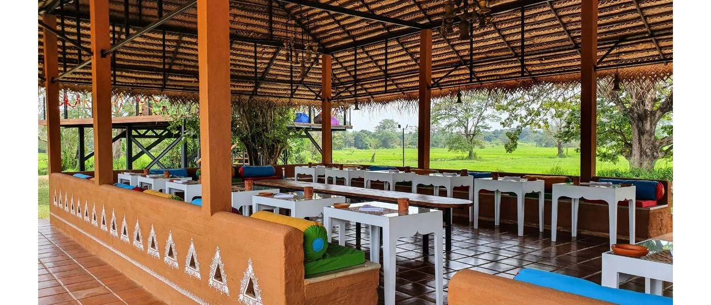 Open-air restaurant pavilion with a thatched-roof and tiled floors, plus white tables arranged around the room in a communal, circle layout