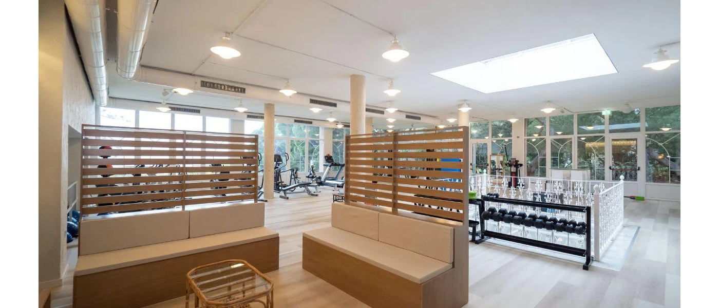 Brightly lit gym with treadmills, bikes and weights, plus a wooden seating area with white cushions