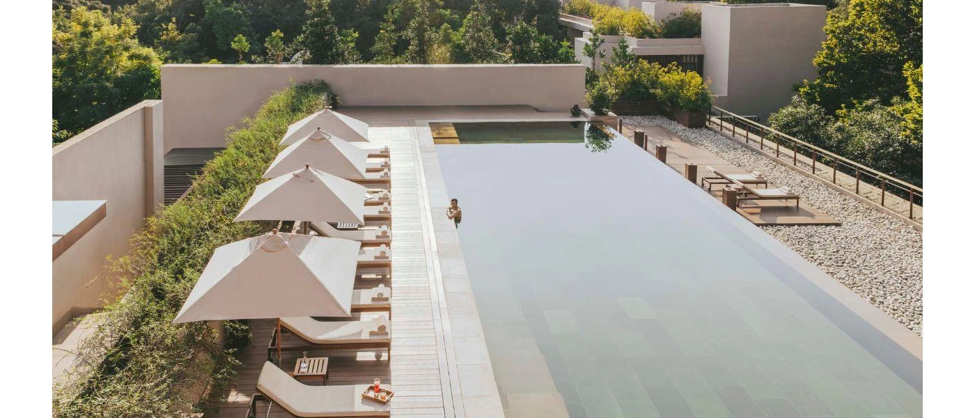 Man relaxes in a rectangular swimming pool lined with smart white-cushioned loungers and parasols