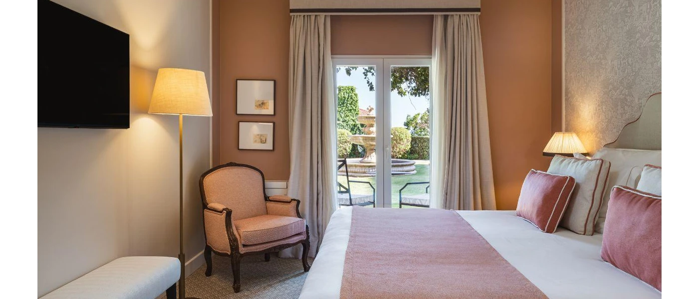 Room with white and caramel walls, white bedding with lilac cushions and throw, a wall-hung and patio doors that open onto a balcony