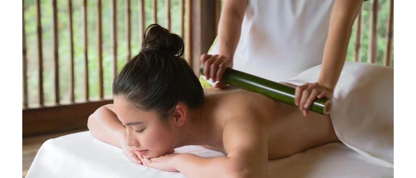 Woman with hair tied in a high bun lies on her arms on her front as a therapist soothes her back with a circular tool