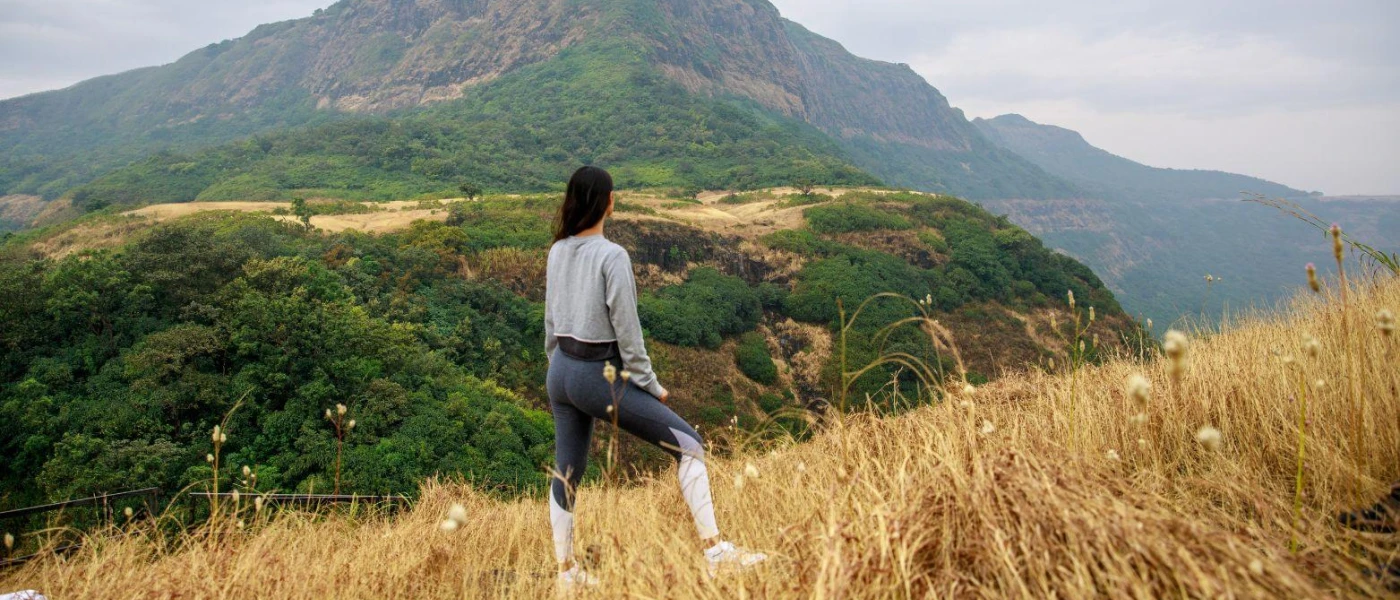 Woman stands on a hillside in active wear, gazing out towards forested peaks