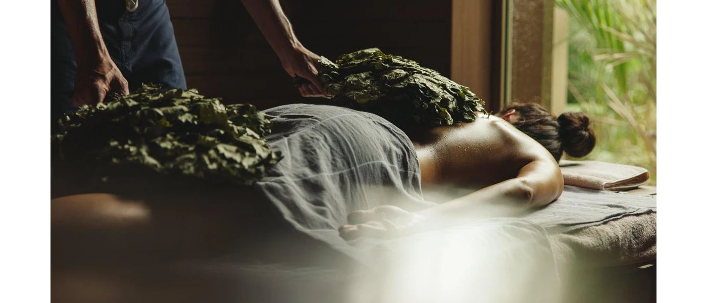 Woman lying on her front on a treatment bed as a therapist works on her using large leaf-like looking items