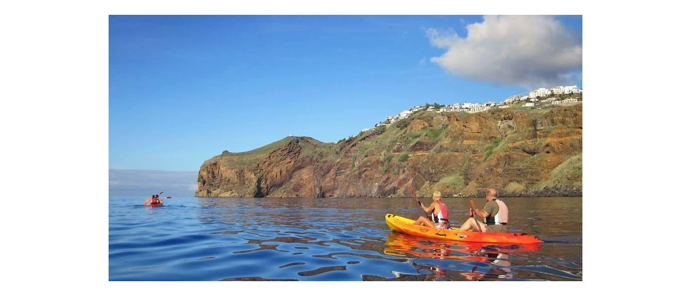 Two people in a yellow and red canoe paddling past a rocky outcrop under a blue sky