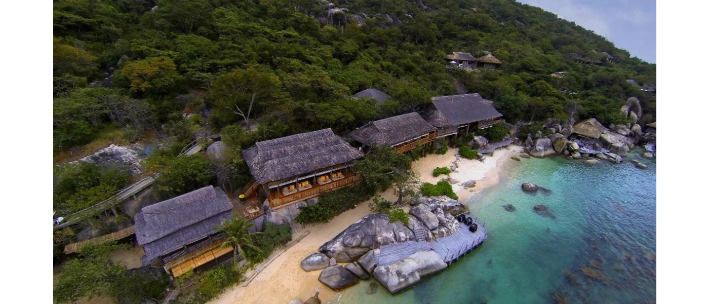 Thatched-roof buildings on top of a white sandy beach, with striking rock formations and turquoise shallows 