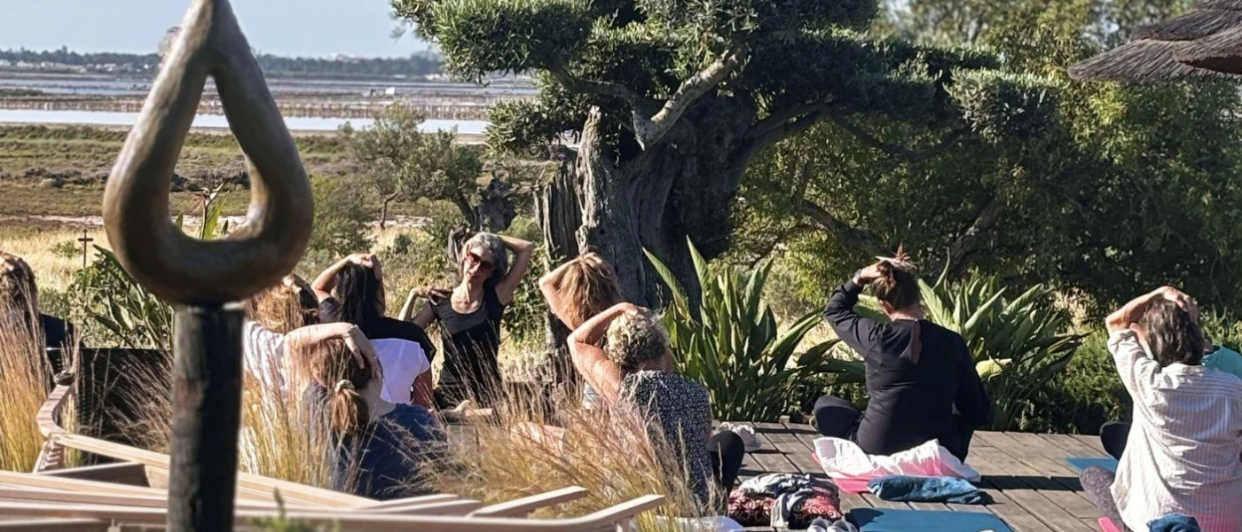 Group sit outside on cushions with their hands on their heads, surrounded by greenery