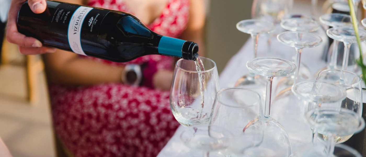 Waiter pours white wine into a glass in front of a woman wearing a red patterned dress