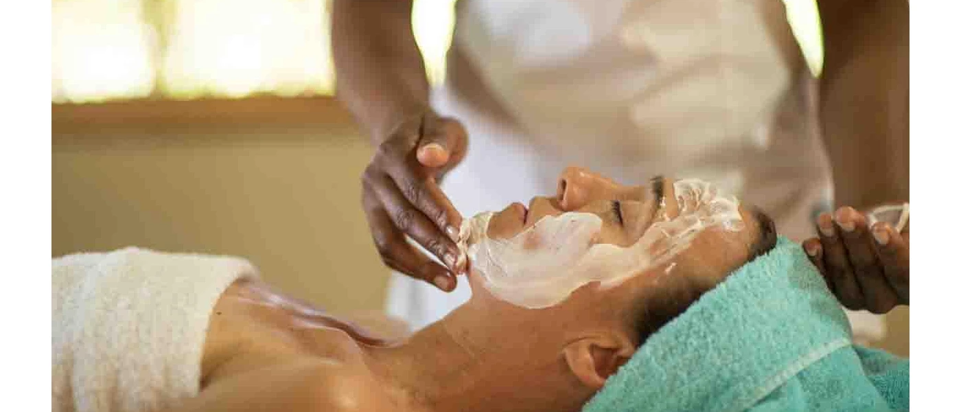 Woman lying down in a towel while a figure in white applies white cream to her face