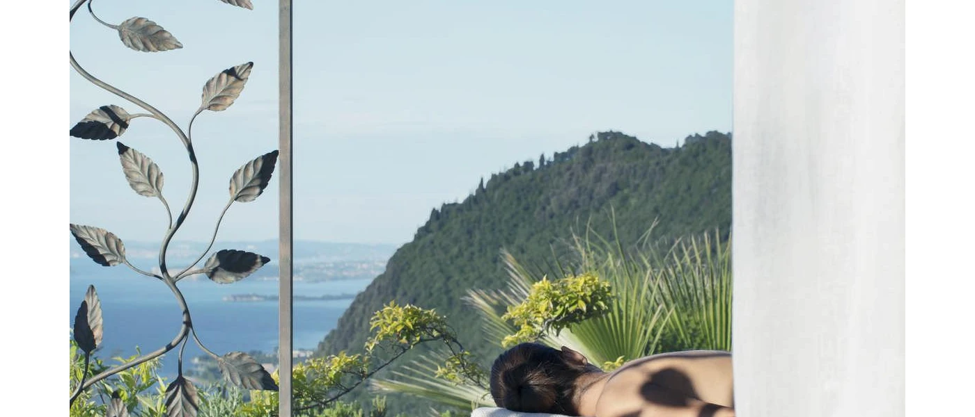 Woman lying down in the sunshine on a massage bed overlooking a lake and green mountains
