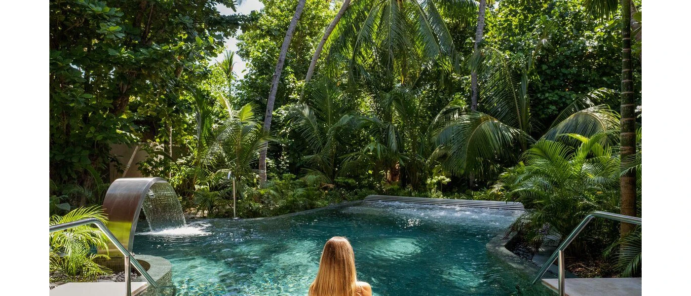 Grotto-like pool with a water jet surrounded by glossy jungle greenery