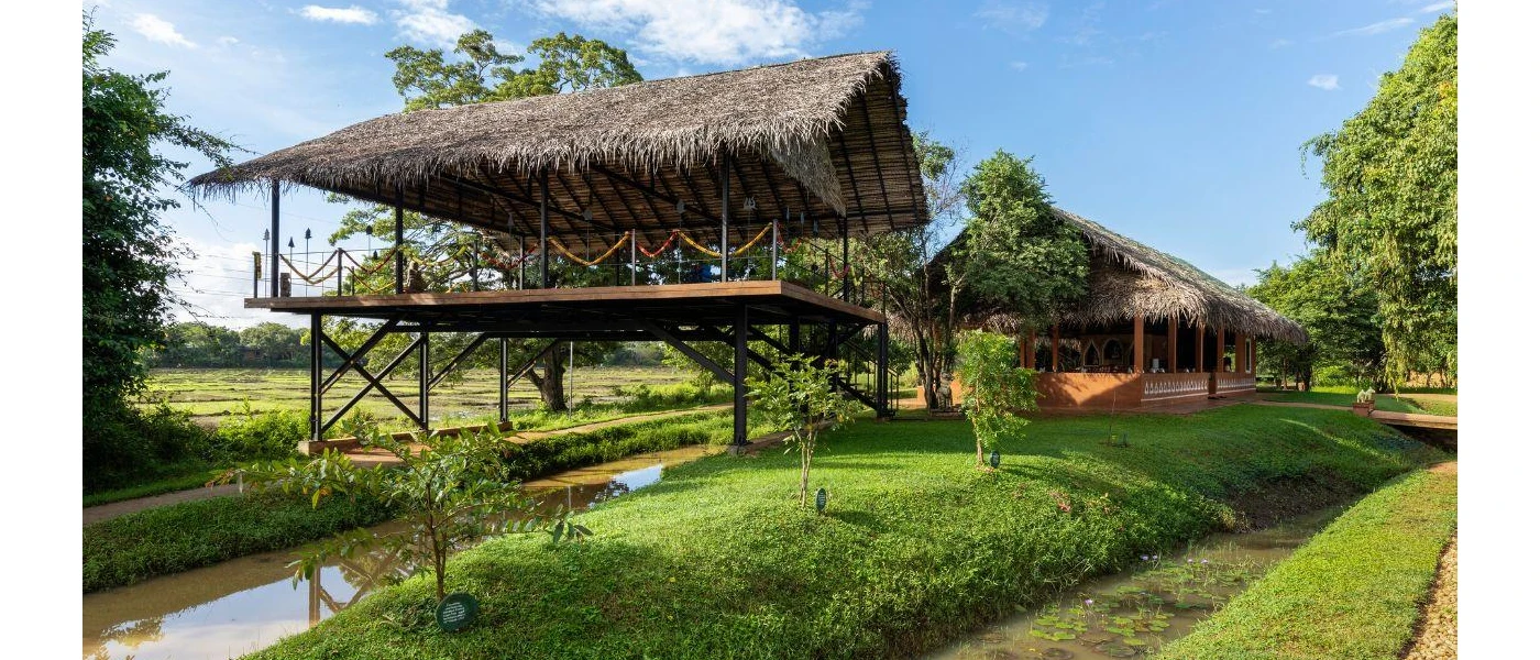 Thatched-roof open-air pavilion, on wooden stilts above a stream and surrounding lawn