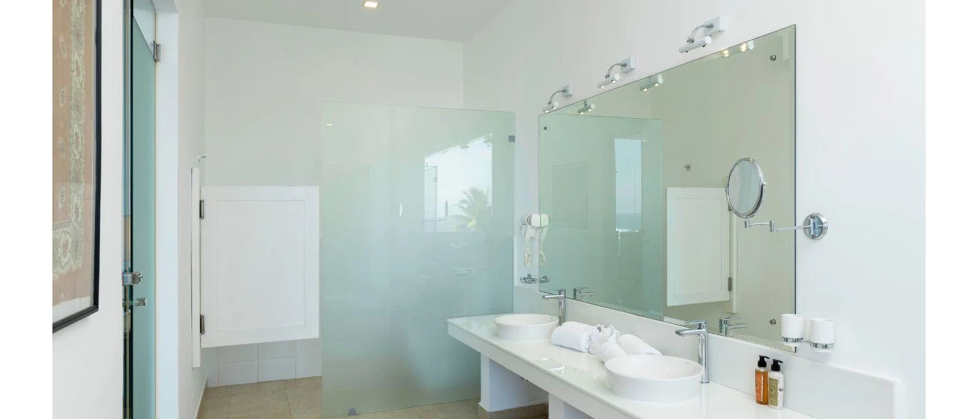 Bathroom with white walls, a large mirror, white vanity unit with twin sinks, a walk-in shower and white towels