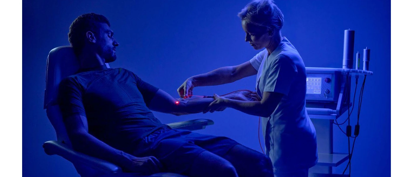 Medical team member inserts an IV into a man's arm with red light technology, in a darkened blue-lit room