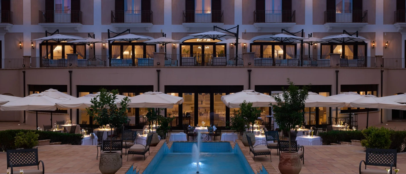 Turquoise pool in a paved terrace with terracotta plant pots in front of a multi-storey building with black window shutters
