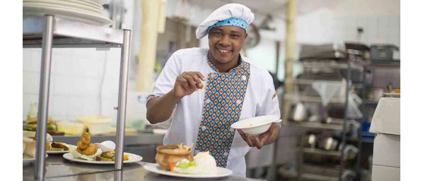 Smiling chef in uniform seasoning a dish in his kitchen