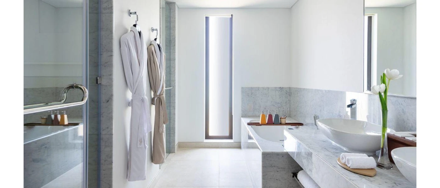 Marble-look bathroom with a glass-doored shower, tub, vanity unit with dual sinks and robes hanging to one side