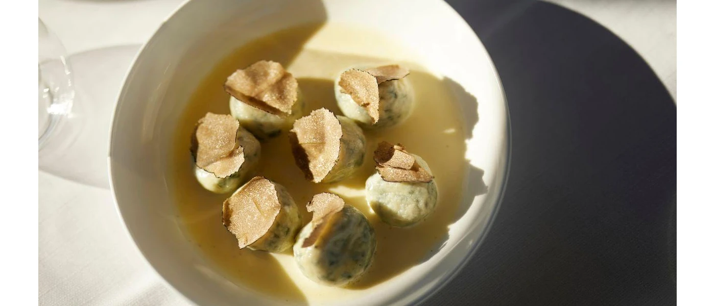 White bowl of broth and circular ingredients topped with truffle shavings