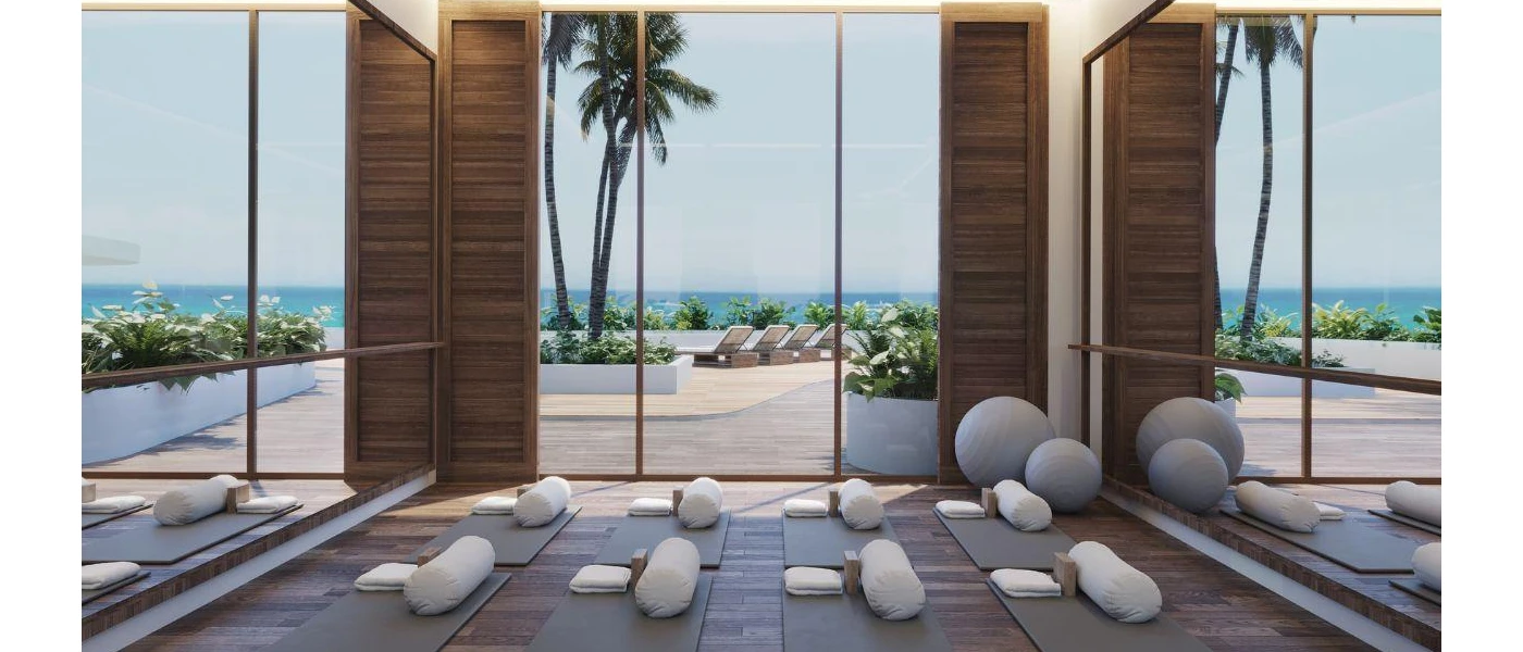 Empty glass-doored studio overlooking a pool terrace, with mats, cushions and white towels laid out ready for a class