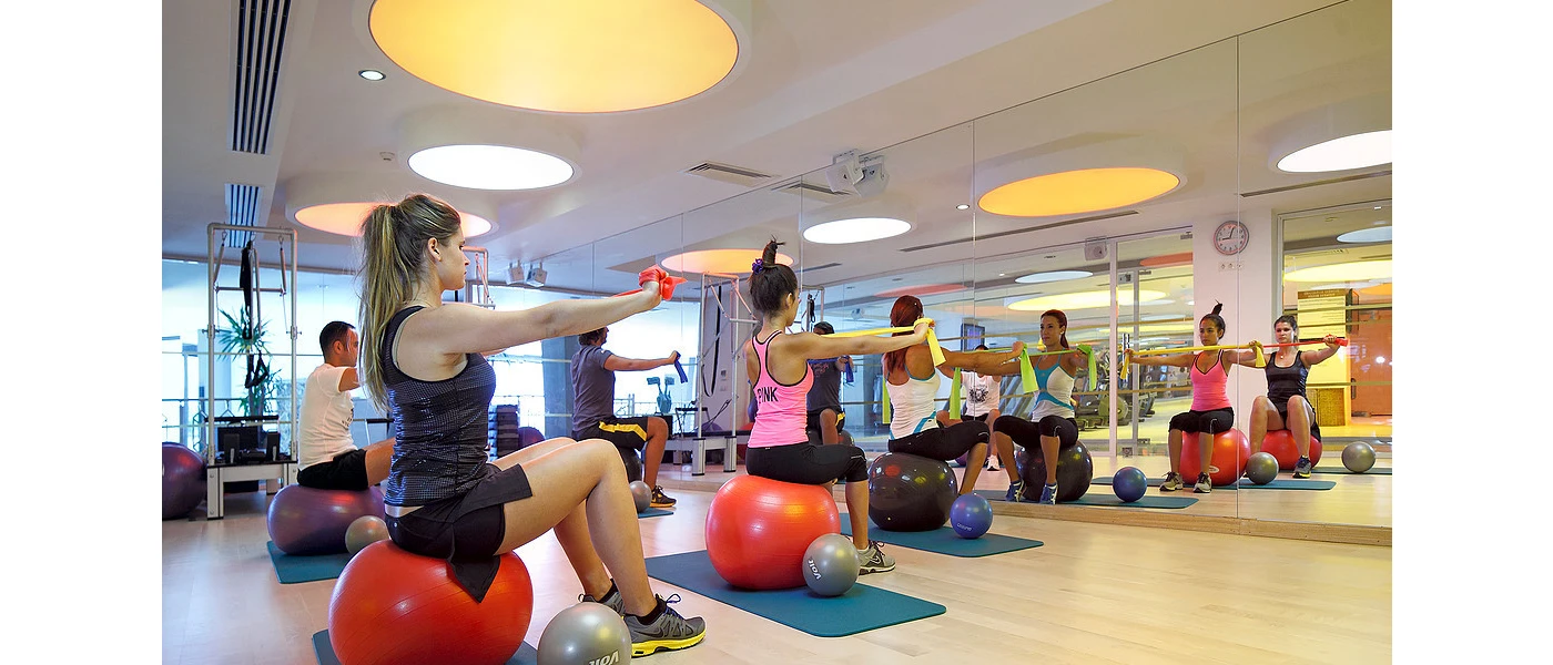 Group in active wear sit on red exercise balls in a studio with a large mirror