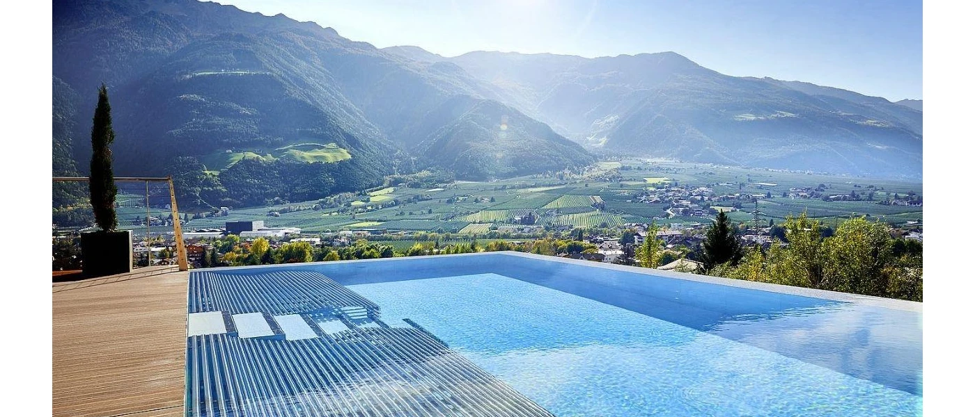Infinity pool with a wooden deck and cypress tree overlooking mountains and valleys under a sunny sky