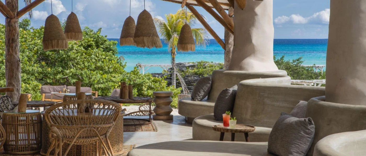 Bohemian seating area with rattan lanterns and chairs, circular cushioned seating and a view of the ocean 