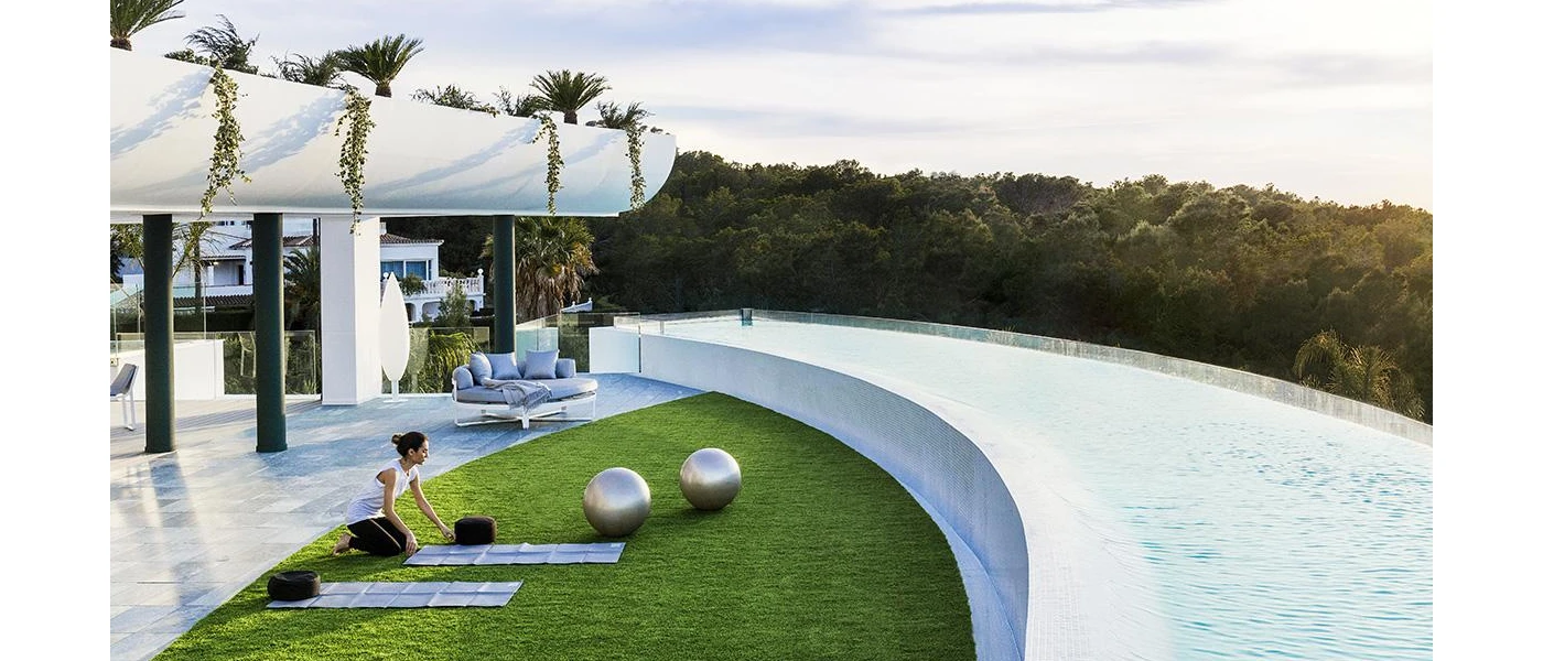 Woman leans on a grass lawn covered with yoga mats and exercise balls on a hilltop terrace