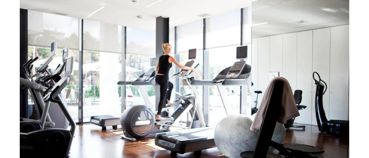 Woman in black works out on a machine in a gym with full-length windows, bikes, treadmills and an exercise ball