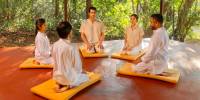 A group meditation in the open shala where guest sit on yellow cushions with their eyes closed 
