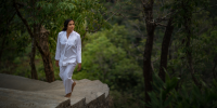 Woman in white strolls up a stone staircase surrounded by forest greenery