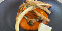 Battered vegetables on an orange puree-like sauce with edible flowers on a dark grey plate