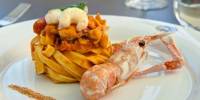 A mound of pasta on a white plate topped with prawns with a prawn that hasn't been shelled to one side