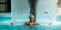 Woman in the thermal pool standing under a fountain of water