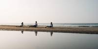 Three people in white practice yoga on the beach under a morning sky