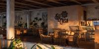 Su Casa restaurant at Palmaïa – The House of AïA Rustic restaurant with beige walls, rattan chairs, macrame designs and plants, and the words 'Su Casa' etched on the wall