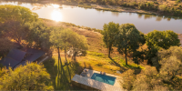 Swimming pool as seen from above, surrounded by greenery and with a river in the background