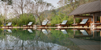Swimming pool lined with white loungers and surrounded by greenery
