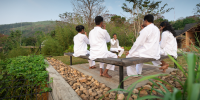 Group in white sits on a bench in an outdoor courtyard overlooking green hills